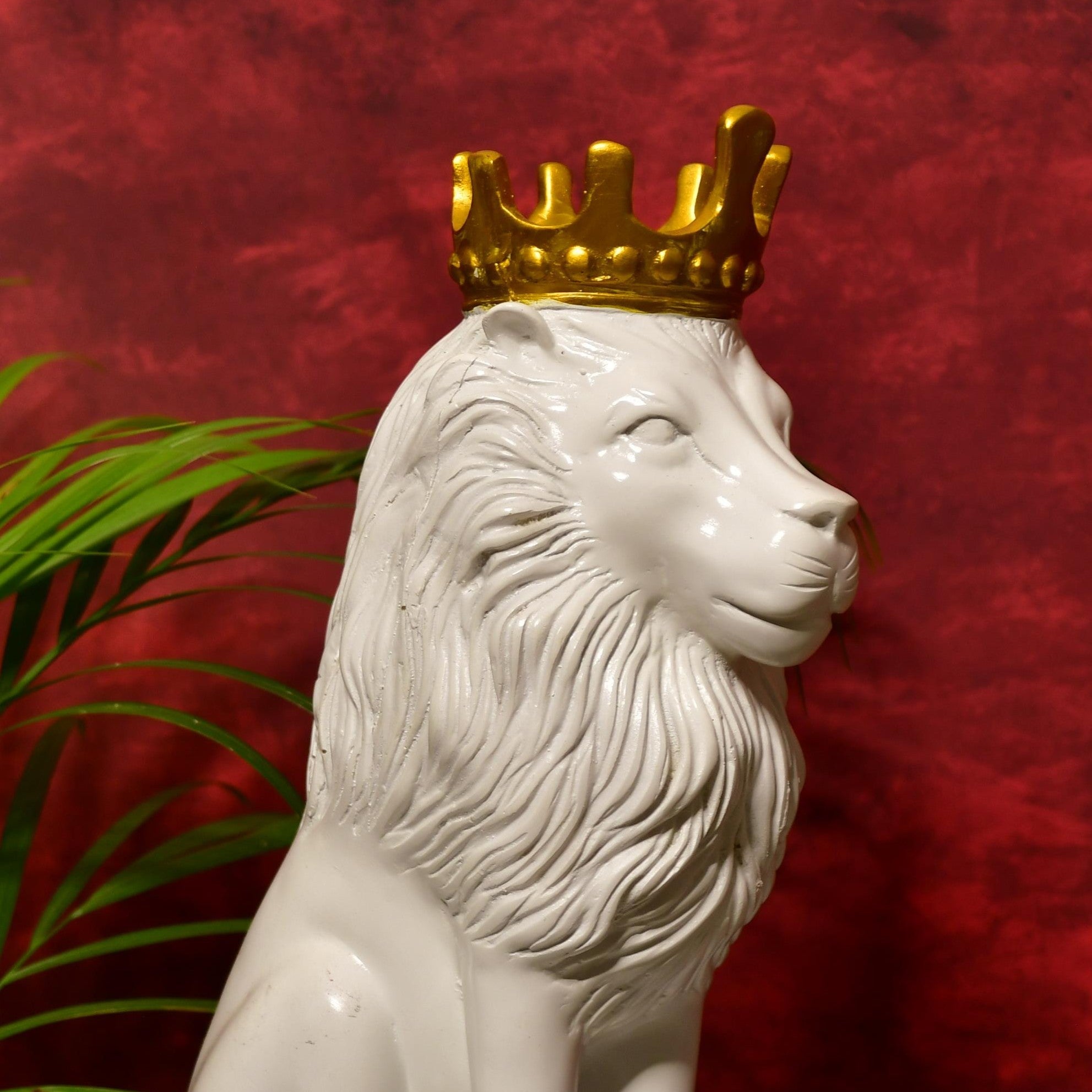 MAYII white lion figurine with detailed mane and gold crown on red background next to green plant