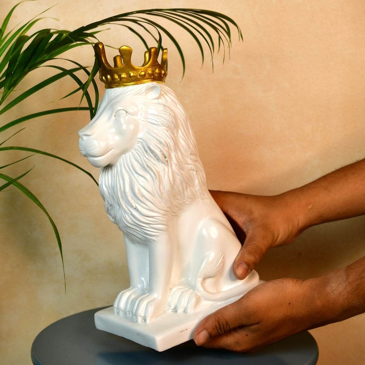 MAYII white lion figurine with golden crown being held over a table with green plant background