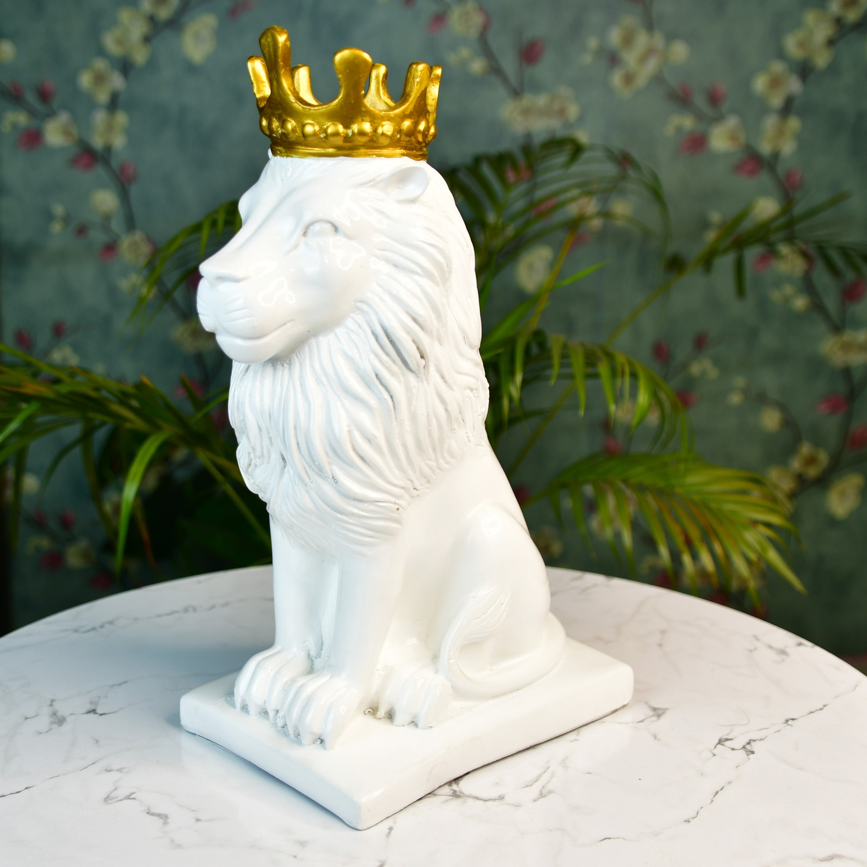 MAYII white lion figurine with a golden crown sitting on a white marble tabletop with plants in the background